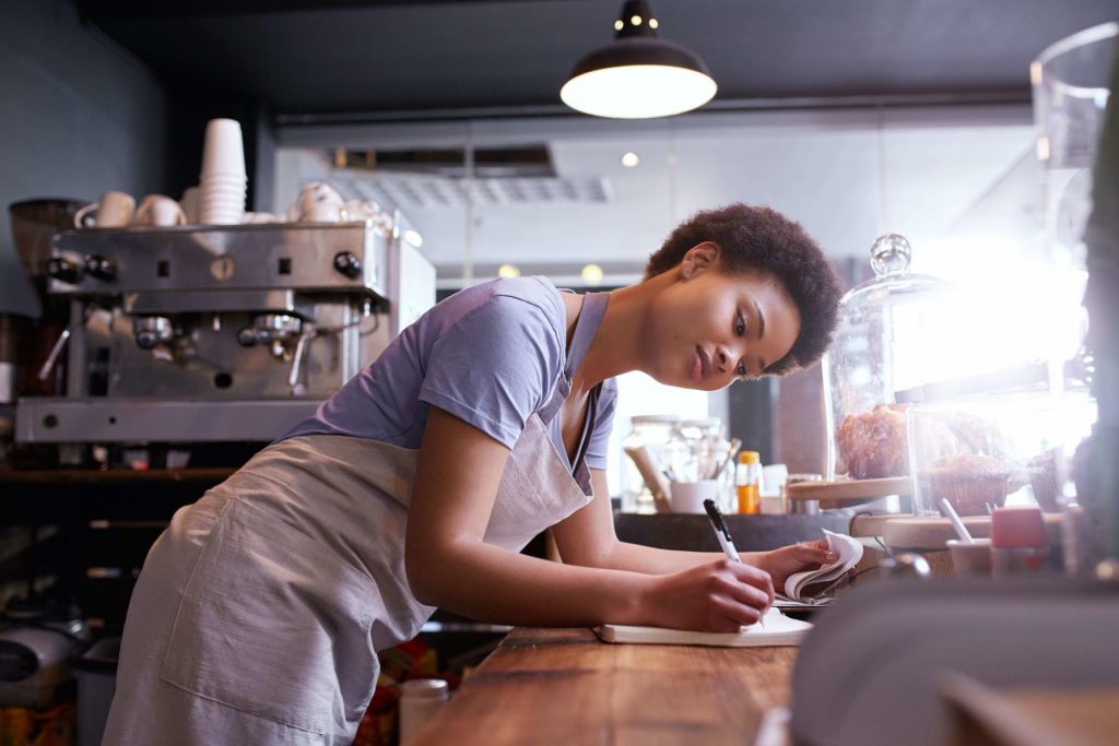 A young woman working at a cafe leaning on a counter doing some admin work